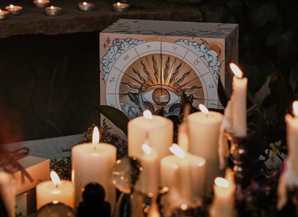 A mystical scene unfolds with a variety of lit candles in front of an Advent Box, its ornate eye design encircled by astrological symbols. The ambiance is warm and mysterious, with dim lighting enhancing the box and candles—a true reflection of the awe-inspiring vibe leading to 2024.