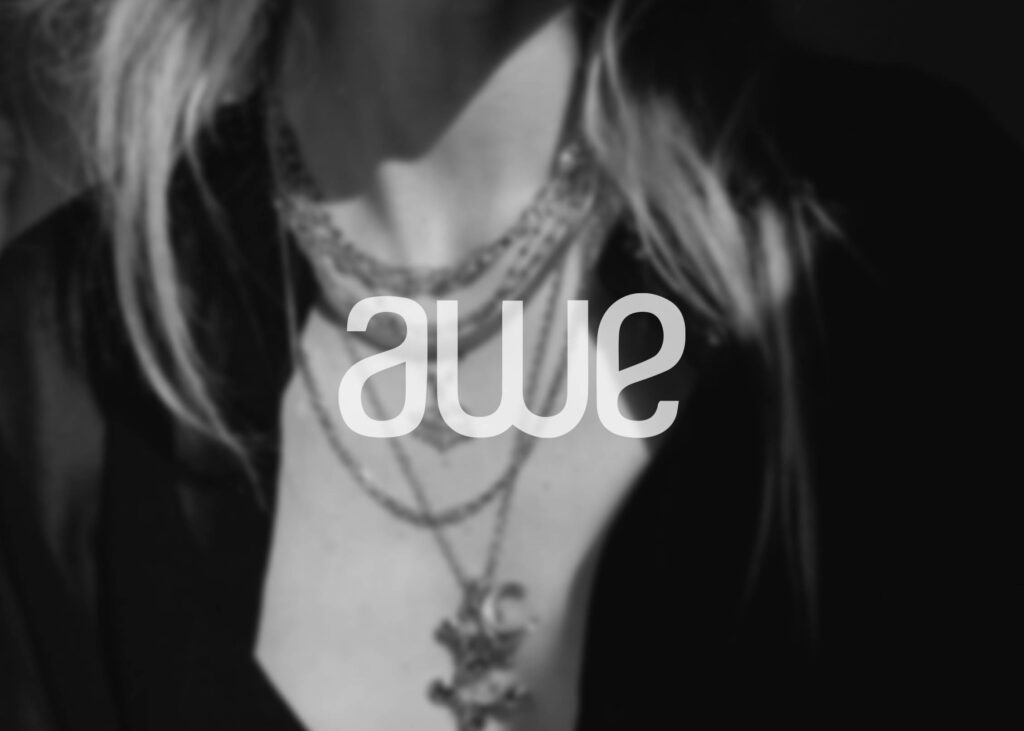 A grayscale image features a person adorned with layered necklaces, with "AWE 2024" boldly displayed in the center. The blurred background accentuates both the striking jewelry and the captivating text.